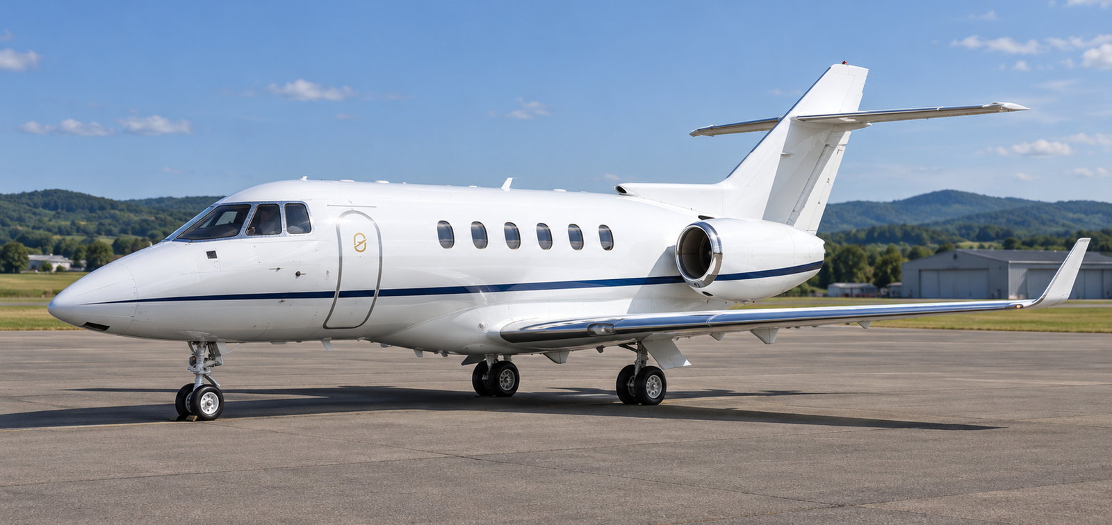Hawker 900XP midsize jet parked on grass edged tarmac with hills behind