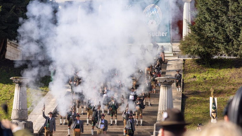 Riflemen in Bavarian dress firing a salute in a cloud of smoke on the steps below the Bavaria statue in Munich