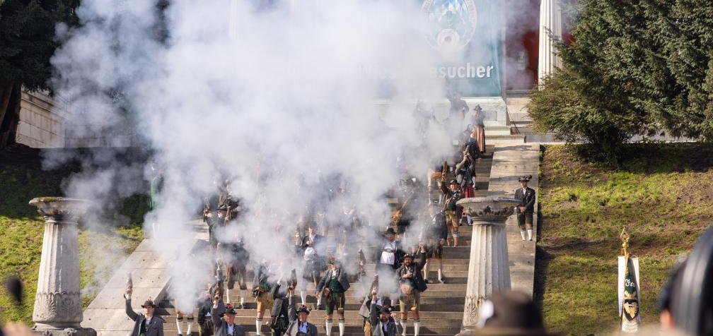 Riflemen in Bavarian dress firing a salute in a cloud of smoke on the steps below the Bavaria statue in Munich