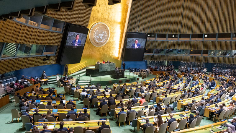 The United Nations General Assembly hall in session, delegates at their desks below the gold emblem