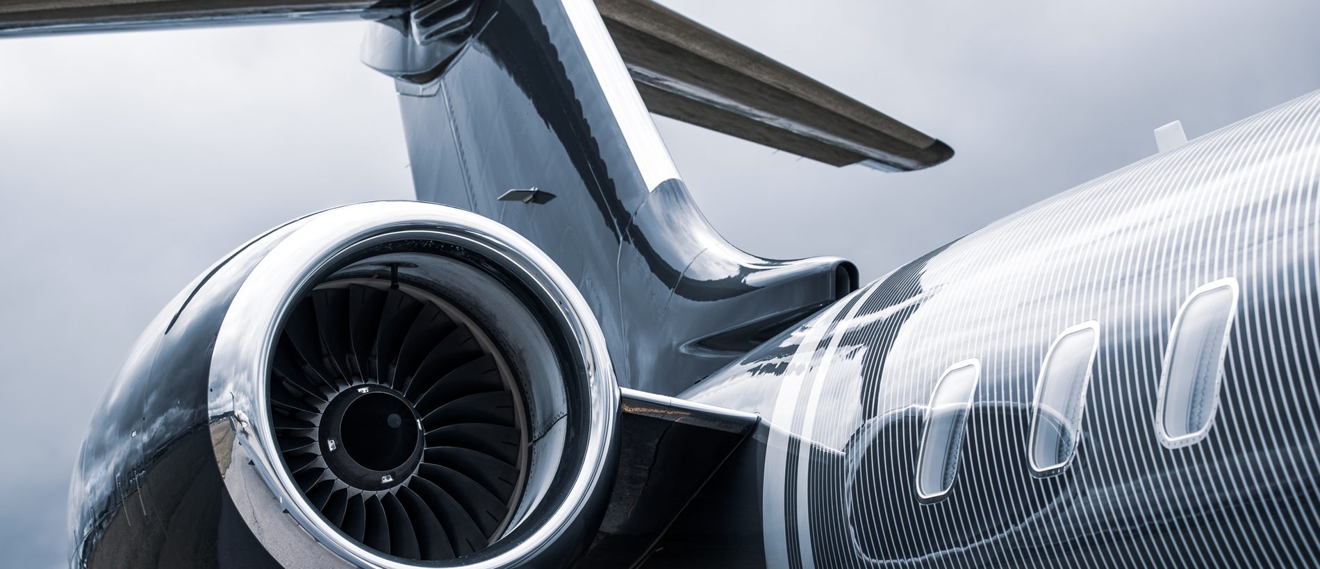 The engine and tail of a dark business jet under an overcast sky