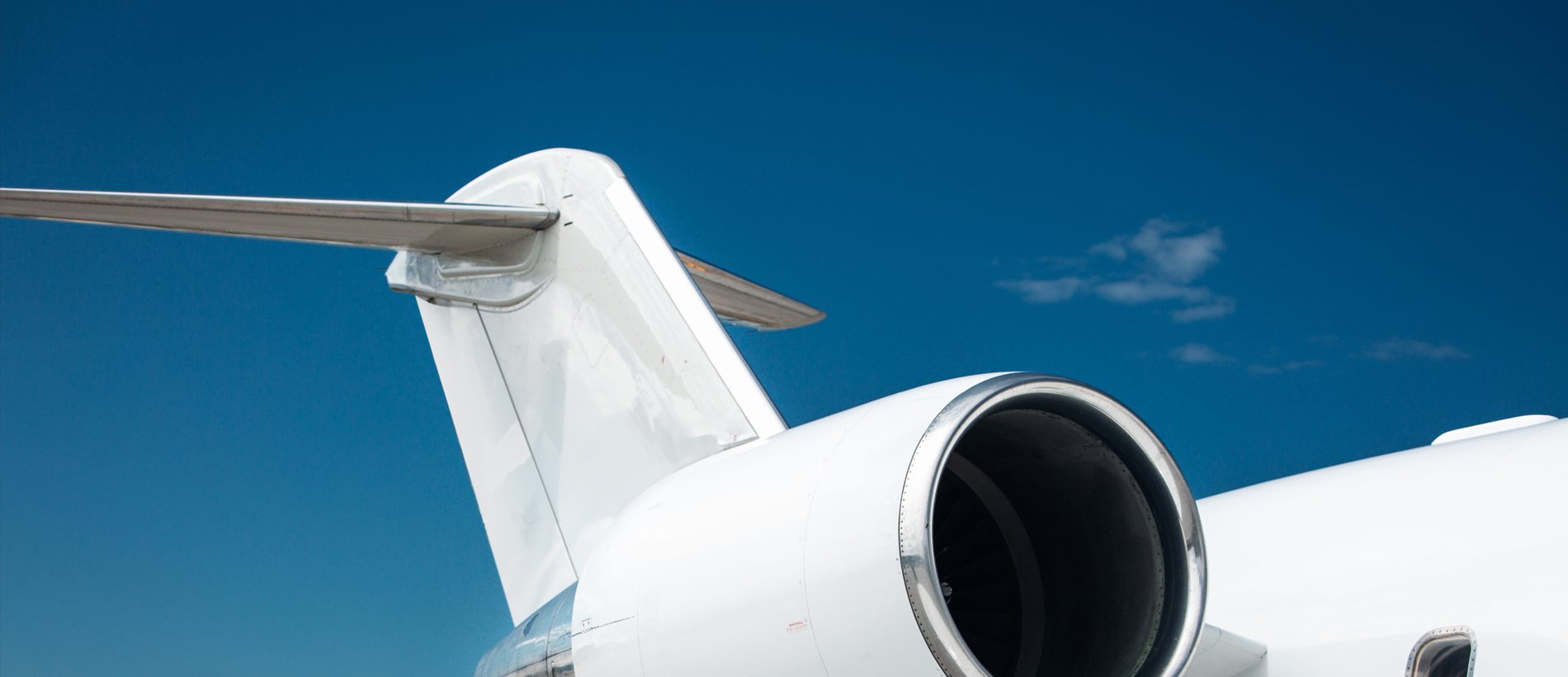 The tail and engine of a white business jet against a blue sky