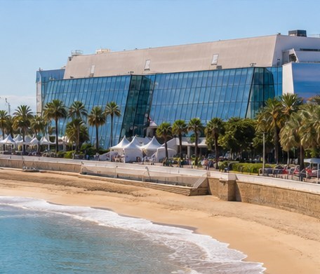 The glass festival hall on the seafront at Cannes, palms and marquees along the beach in front of it