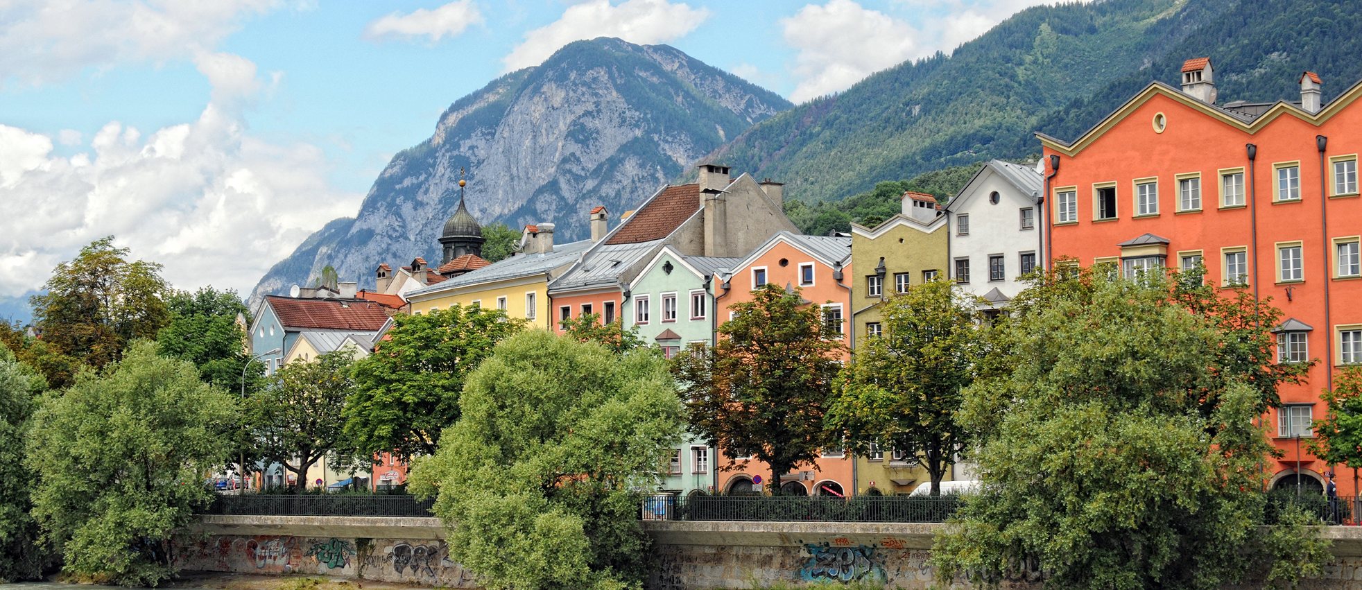 Rows of painted houses along the river Inn in Innsbruck, with the mountains of the Nordkette behind